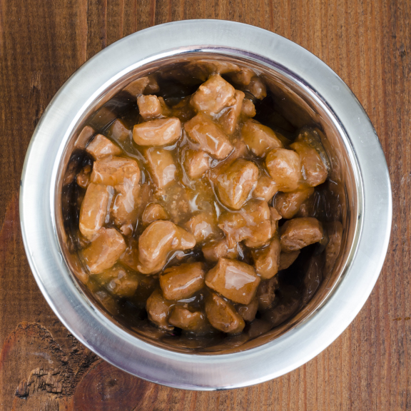 Metal bowl filled with a gravy-style wet food on a wooden background.